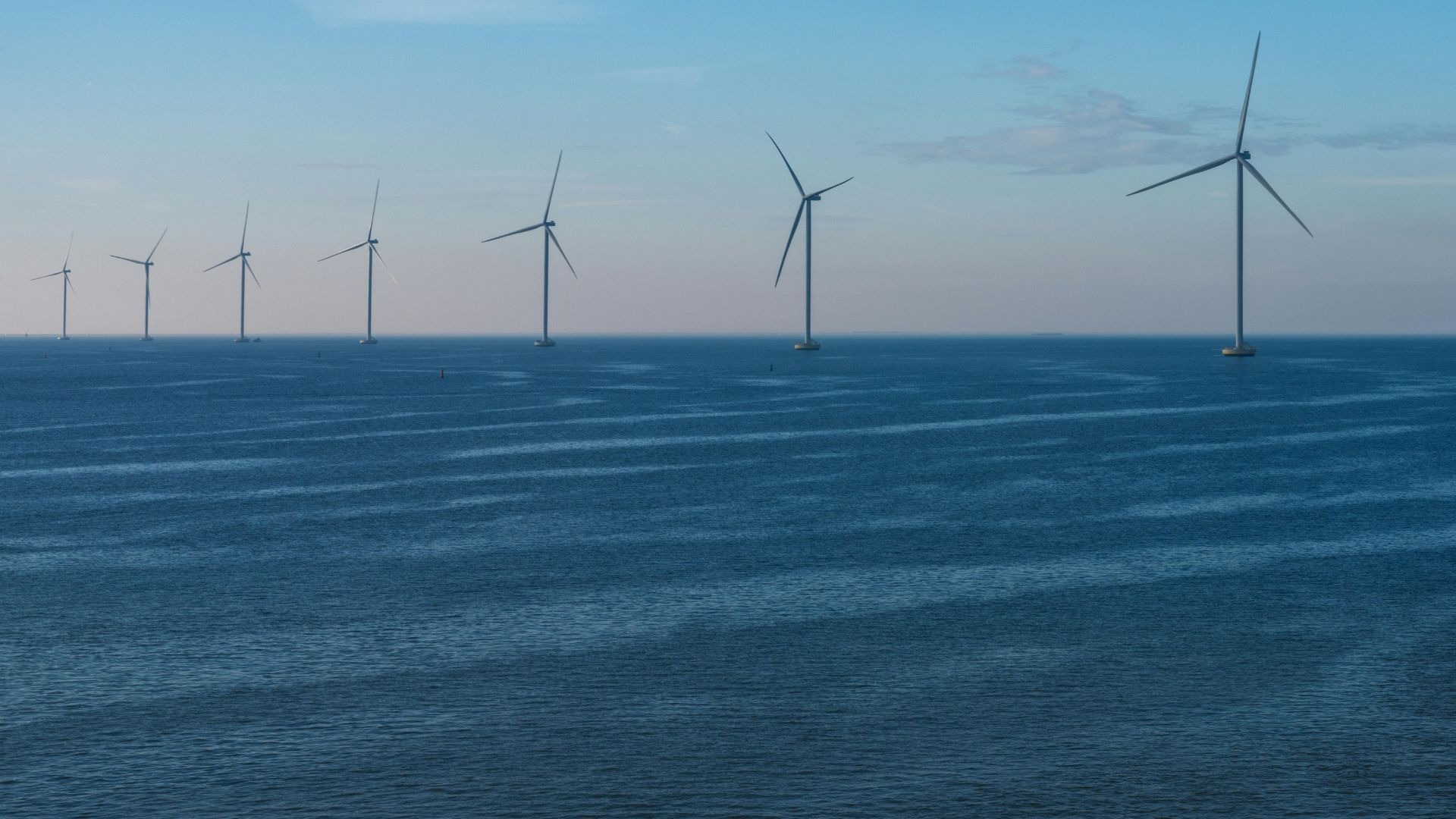 Parque eólico marino con aerogeneradores sobre un mar en calma al atardecer