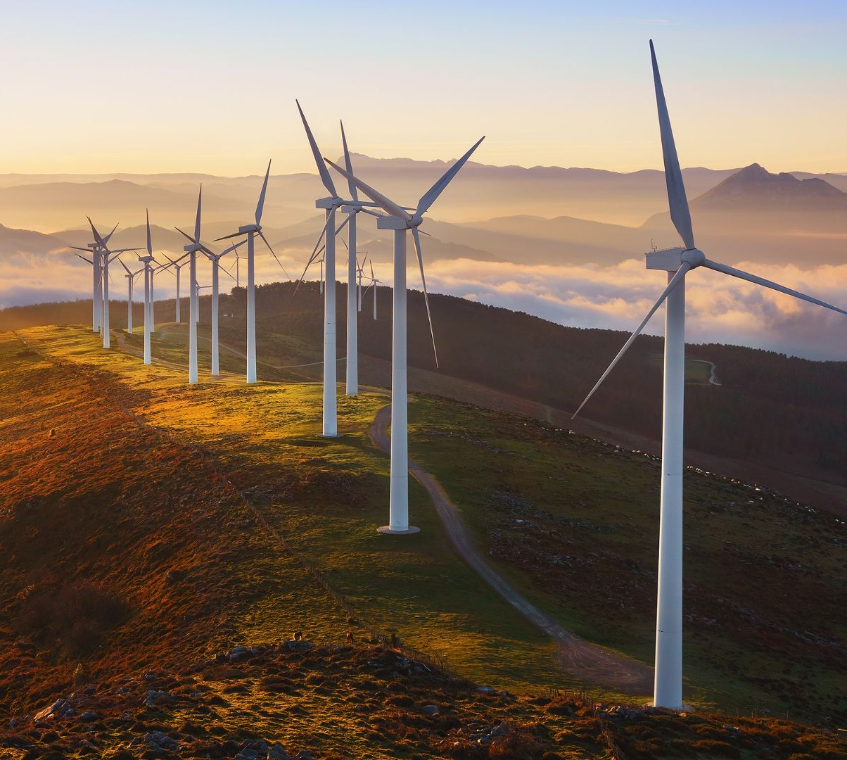 Hilera de aerogeneradores en una cresta montañosa al atardecer, con nubes bajas en el valle
