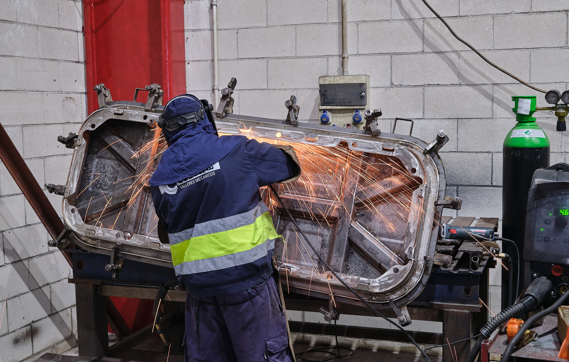 Operario puliendo una escotilla naval sobre su bancada de trabajo, con chispas, en el taller de EPER Group Fene