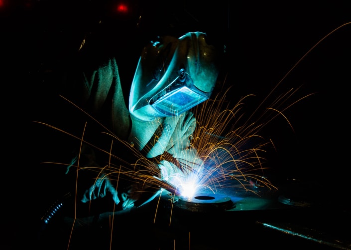 Soldador trabajando con chispas y luz azul sobre una pieza metálica