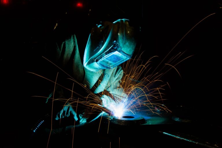 Soldador con careta trabajando una pieza metálica entre chispas