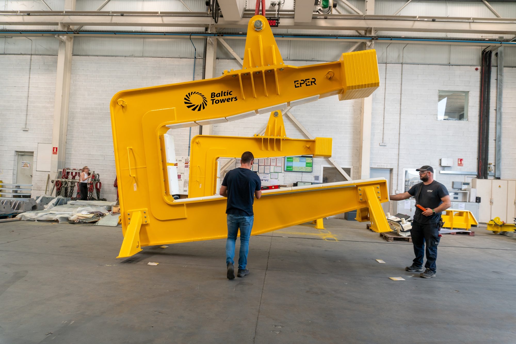 Dos operarios junto a un útil de elevación amarillo suspendido en una nave industrial